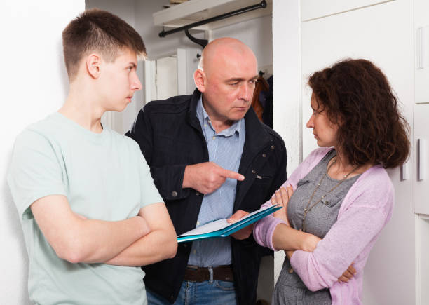 Семейная дискуссия, где пожилой мужчина указывает на документ, который держит женщина, а молодой человек наблюдает за ним на кухне.